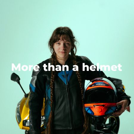 Young woman wearing safety gear poses with a motorcycle helmet under her arm. Captions 'More than a helmet'